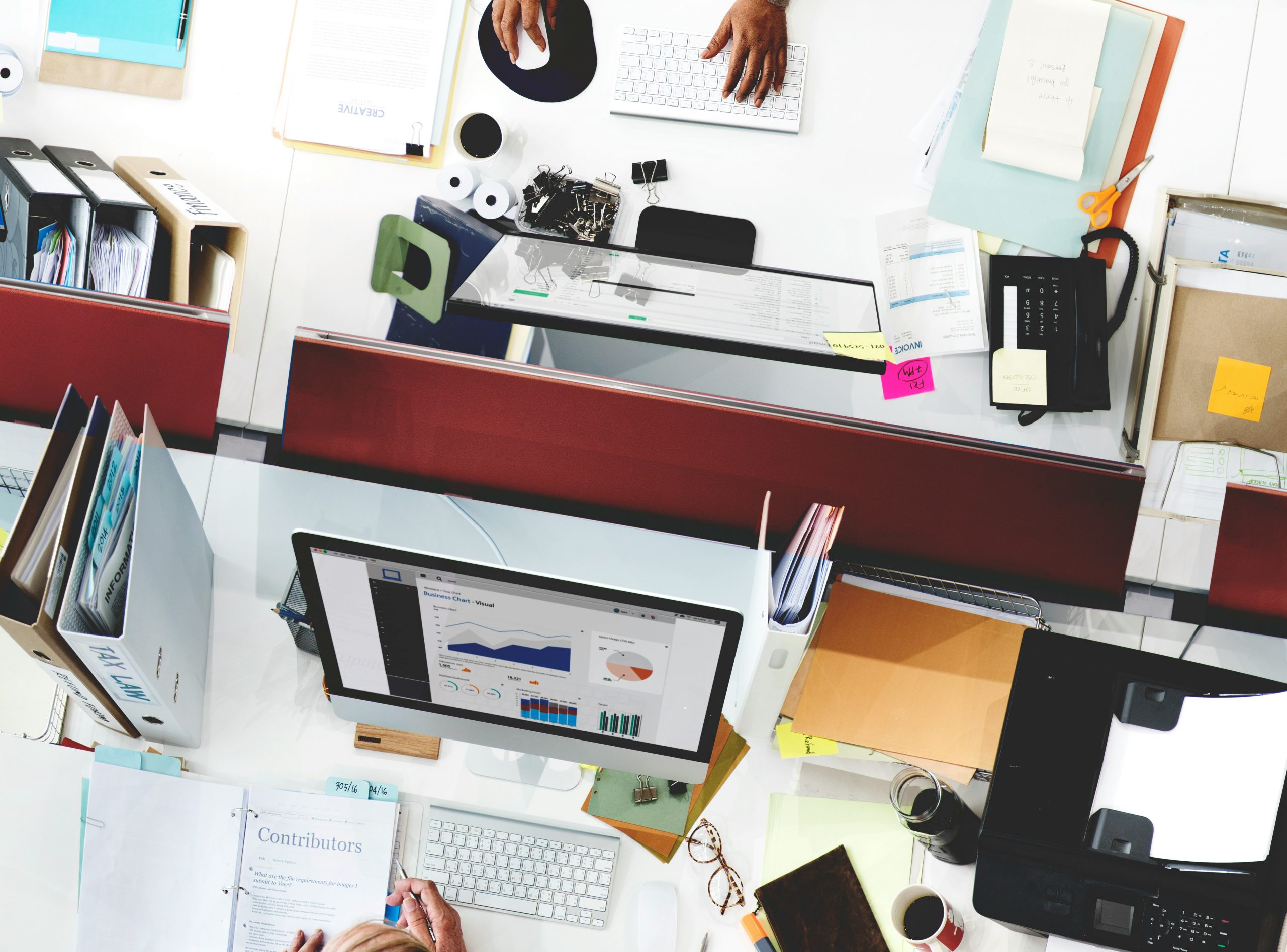 enterprise-ai-agents-platform-decision-busy-office-desks Overhead view of multiple office desks and screens showing a busy operating environment.